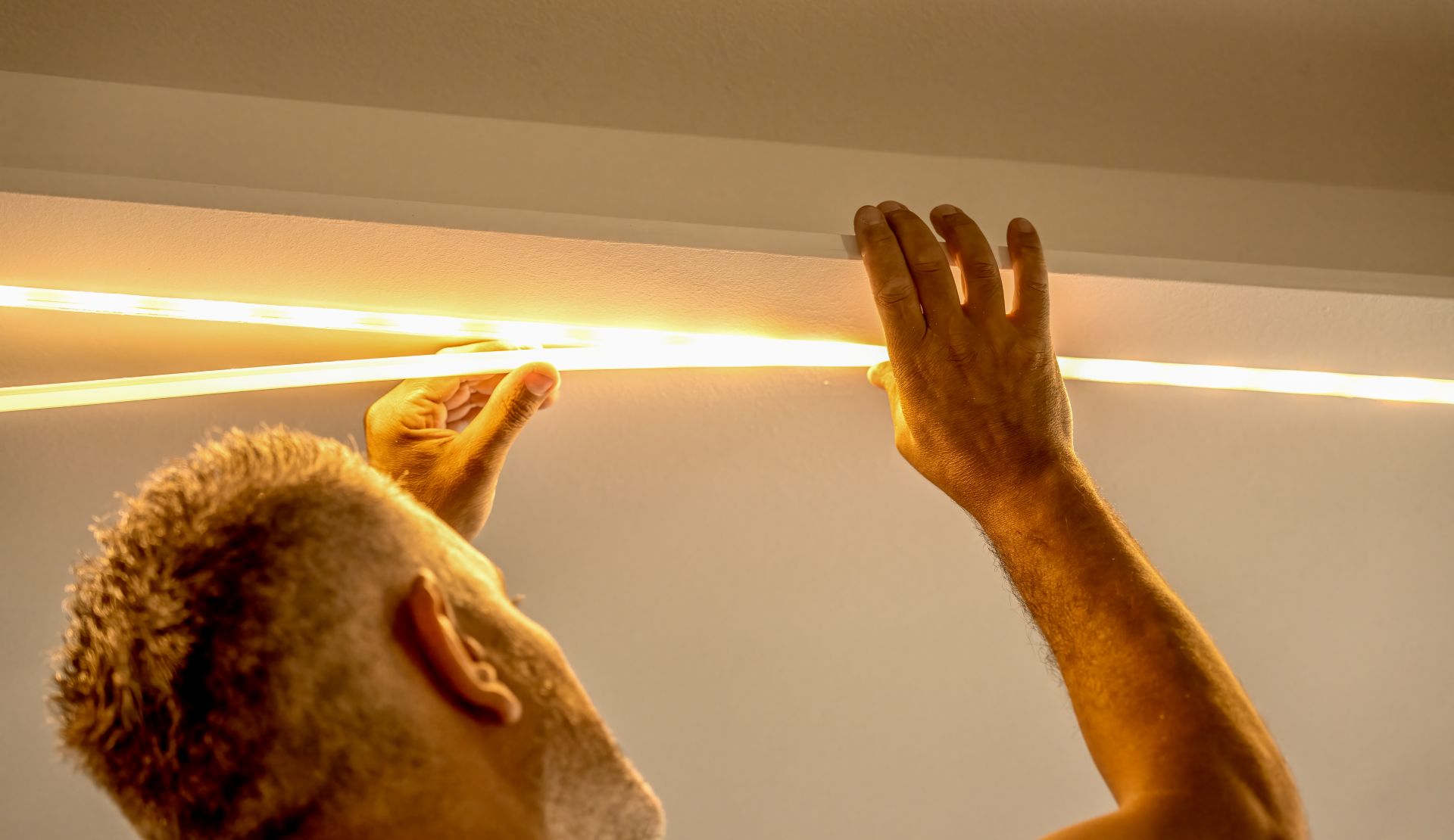 Mann befestigt LED Strip an einer Zimmerdecke – werkzeuglose DIY-Lichtinstallation mit indirekter Beleuchtung